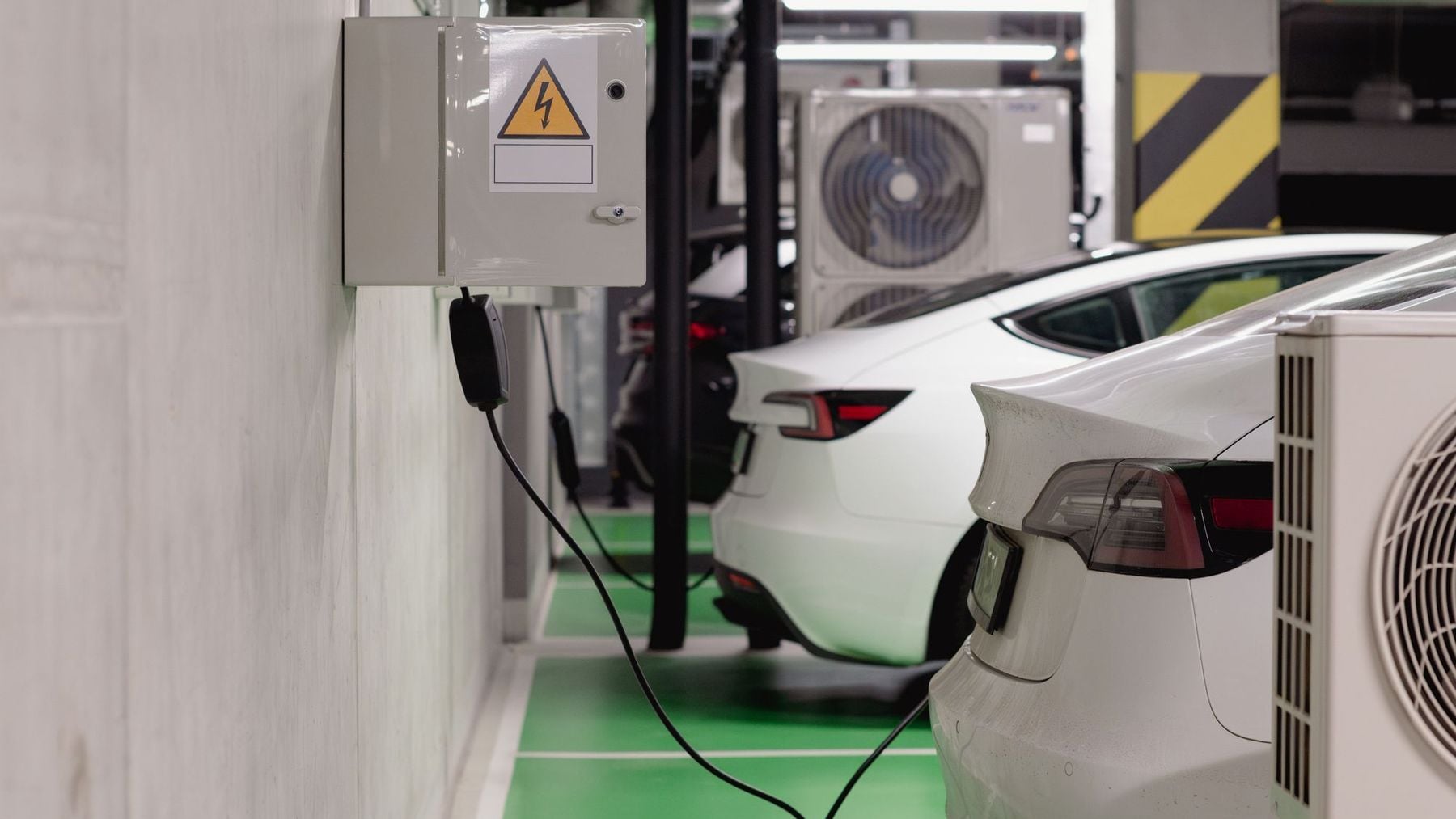 Carro elétrico carregando em garagem subterrânea de condomínio, com quadro elétrico na parede — cenário regulado pela NT 23 do CBMES