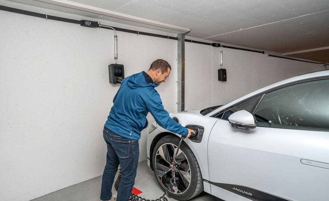 Morador conectando carro elétrico a wallbox instalado na parede da garagem do condomínio — estação em modo 3, admitida no interior da edificação pela NT 23
